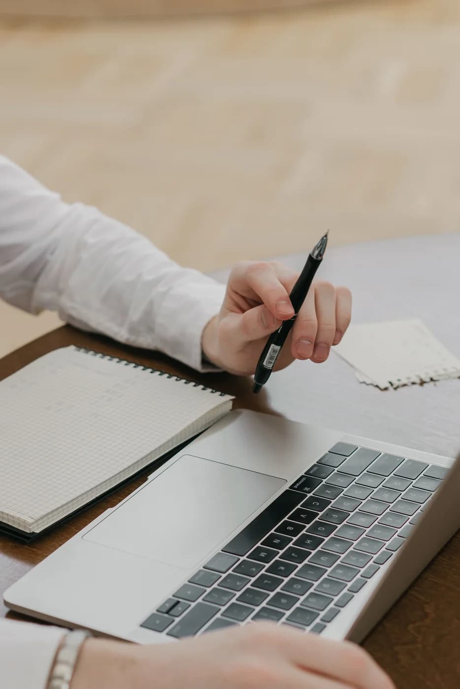 Eine Hand mit Stift über einem Notizblock, davor ein Laptop